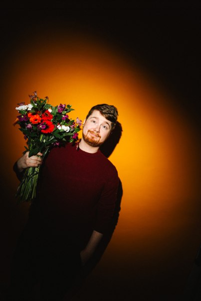 A person holds a colorful bouquet of flowers in front of a bright orange background., &copy; Rosenau Kultur e.V.