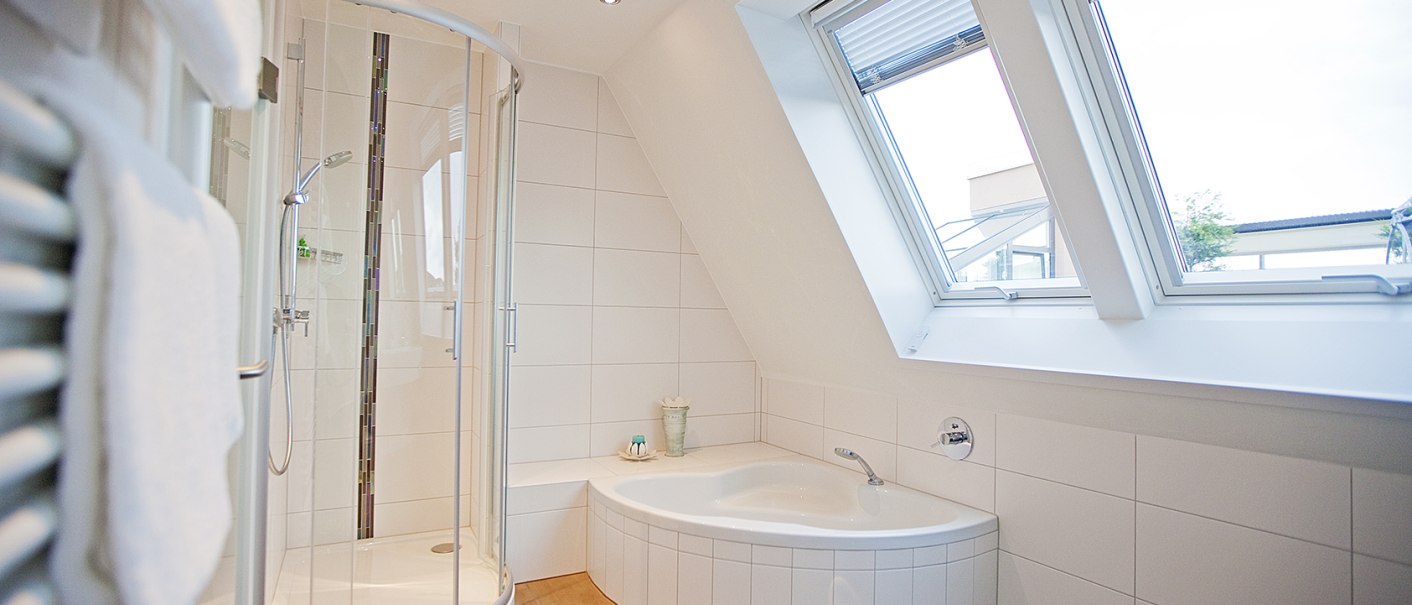 Helles Badezimmer mit Eckbadewanne, runder Duschkabine und gro&szlig;en Dachfenstern. Wei&szlig;e Fliesen und Handtuchhalter an der Wand., &copy; Hotel Krone