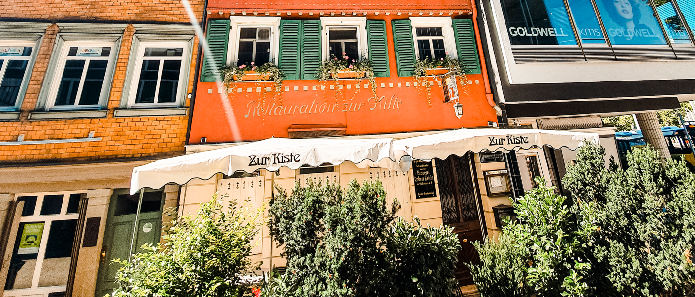 Die Weinstube Zur Kiste mit roter Fassade, grünen Fensterläden und Markise. Pflanzen schmücken den Eingangsbereich., © Stuttgart-Marketing GmbH Die Weinstube Zur Kiste mit roter Fassade, grünen Fensterläden und Markise. Pflanzen schmücken den Eingangsbereich., © Stuttgart-Marketing GmbH