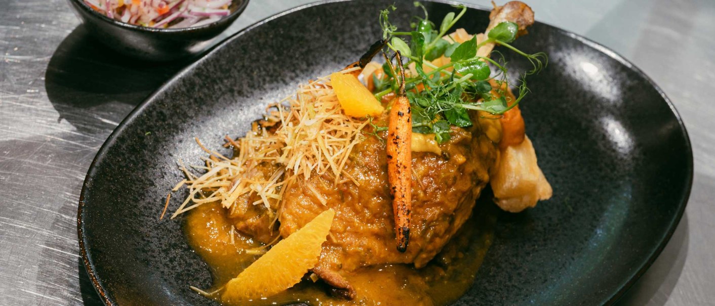 An artfully arranged dish on a black plate, garnished with vegetables, herbs and a sauce. A bowl of salad in the background., © � 2024 Ohh halla, all rights reserved.