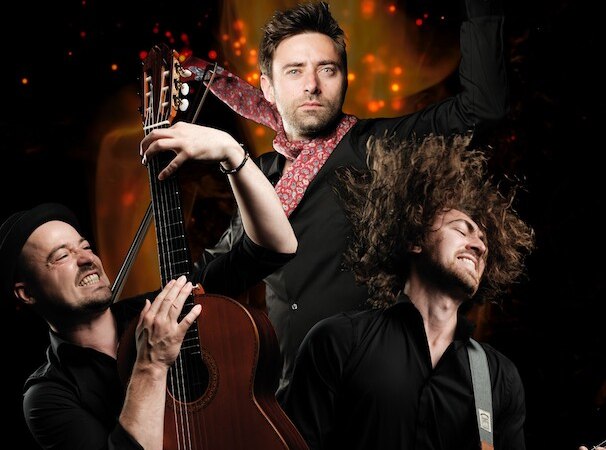 Drei Musiker spielen leidenschaftlich Gitarre und Geige vor einem Hintergrund aus Flammen, was Dynamik und Energie vermittelt., © Theaterhaus Stuttgart e.V. Drei Musiker spielen leidenschaftlich Gitarre und Geige vor einem Hintergrund aus Flammen, was Dynamik und Energie vermittelt., © Theaterhaus Stuttgart e.V.