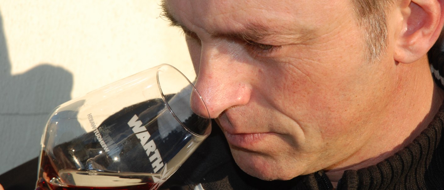 A man smells a glass of red wine labeled 'WARTH' while enjoying the aromas., © Weingut Warth A man smells a glass of red wine labeled 'WARTH' while enjoying the aromas., © Weingut Warth