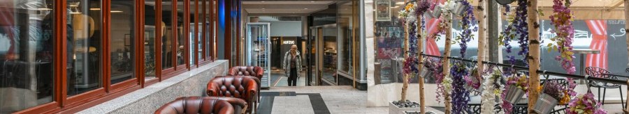 Ein gemütlicher Innenhof mit roten Ledersesseln, dekorativen Pflanzen und einem Glasdach. Eine Person betritt den Bereich im Hintergrund., © SMG, Sarah Schmid