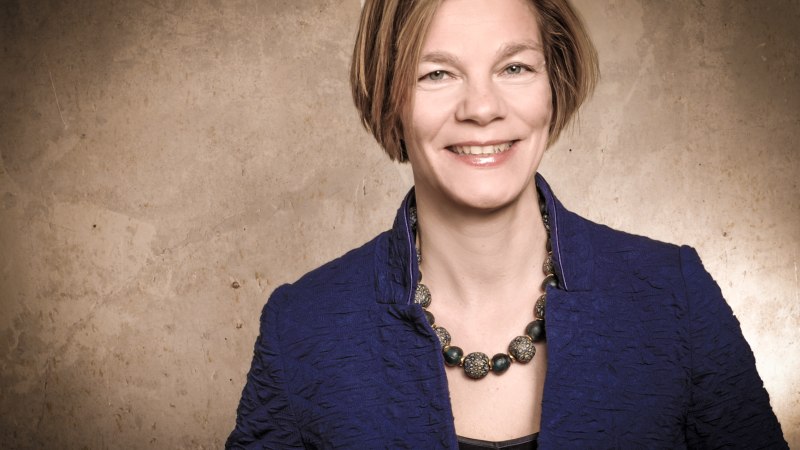 Eine Frau mit kurzem Haar trägt einen blauen Blazer und eine Halskette. Sie lächelt vor einem beigen Hintergrund., © Foto: Tanja Isecke Eine Frau mit kurzem Haar trägt einen blauen Blazer und eine Halskette. Sie lächelt vor einem beigen Hintergrund., © Foto: Tanja Isecke