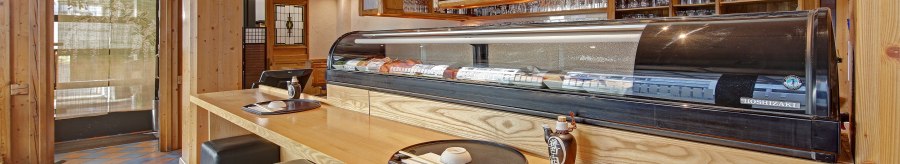 A Japanese restaurant with a sushi counter, bar stools and shelves full of sake bottles. Wooden elements dominate the interior., © Martin Frey