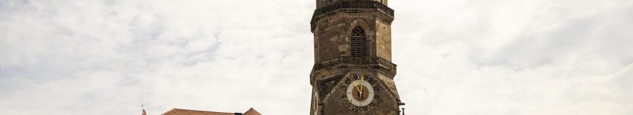 Tower of the collegiate church in Stuttgart with clock and weathercock, surrounded by buildings under a cloudy sky., © SMG Stuttgart Marketing GmbH - Sarah Schmid