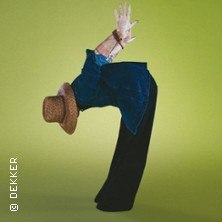 Person in blauer Jacke und Strohhut macht eine R&uuml;ckw&auml;rtsbeuge vor gr&uuml;nem Hintergrund., &copy; links im Bild