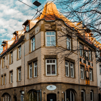 Eckgebäude mit roten Ziegeldächern, verziertem Mauerwerk und großen Fenstern. Ein Baum ohne Blätter steht daneben, blauer Himmel im Hintergrund., © Stuttgart-Marketing GmbH, Sarah Schmid Eckgebäude mit roten Ziegeldächern, verziertem Mauerwerk und großen Fenstern. Ein Baum ohne Blätter steht daneben, blauer Himmel im Hintergrund., © Stuttgart-Marketing GmbH, Sarah Schmid