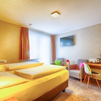 A cozy hotel room with a double bed, desk, TV and two armchairs. Bright curtains and colorful cushions create an inviting atmosphere., &copy; TOMAS
