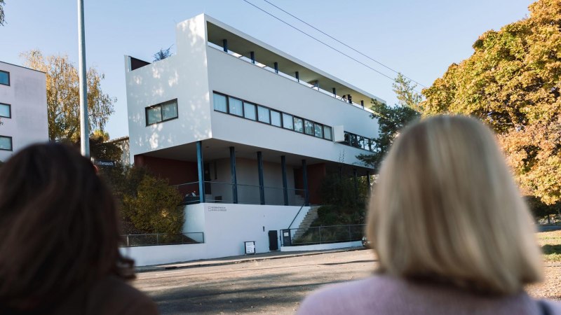 Two people look at the Le Corbusier house in the Wei&szlig;enhofsiedlung. Modern building with clear lines, surrounded by autumnal trees., &copy; Stuttgart-Marketing GmbH, wpsteinheisser