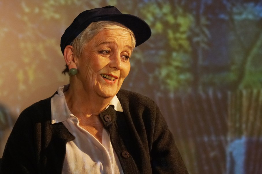 An older woman with a cap and earrings smiles warmly. The background is blurred and shows a natural scene., &copy; Katja Ritter