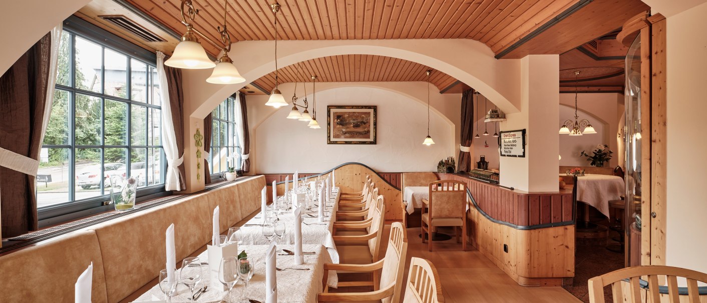 A cozy restaurant with wooden furniture, set tables, and large windows. The ceiling is made of wood, and there are hanging lamps., © Badhotel Restaurant Stauferland A cozy restaurant with wooden furniture, set tables, and large windows. The ceiling is made of wood, and there are hanging lamps., © Badhotel Restaurant Stauferland