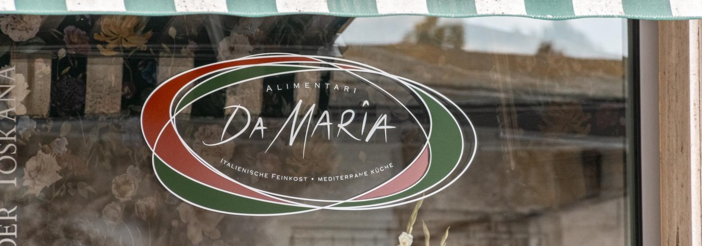 Schaufenster mit dem Logo von "Alimentari Da Maria". Es zeigt italienische Farben und bietet italienische Feinkost und mediterrane K&uuml;che an., &copy; Stuttgart Marketing GmbH, Sarah Schmid