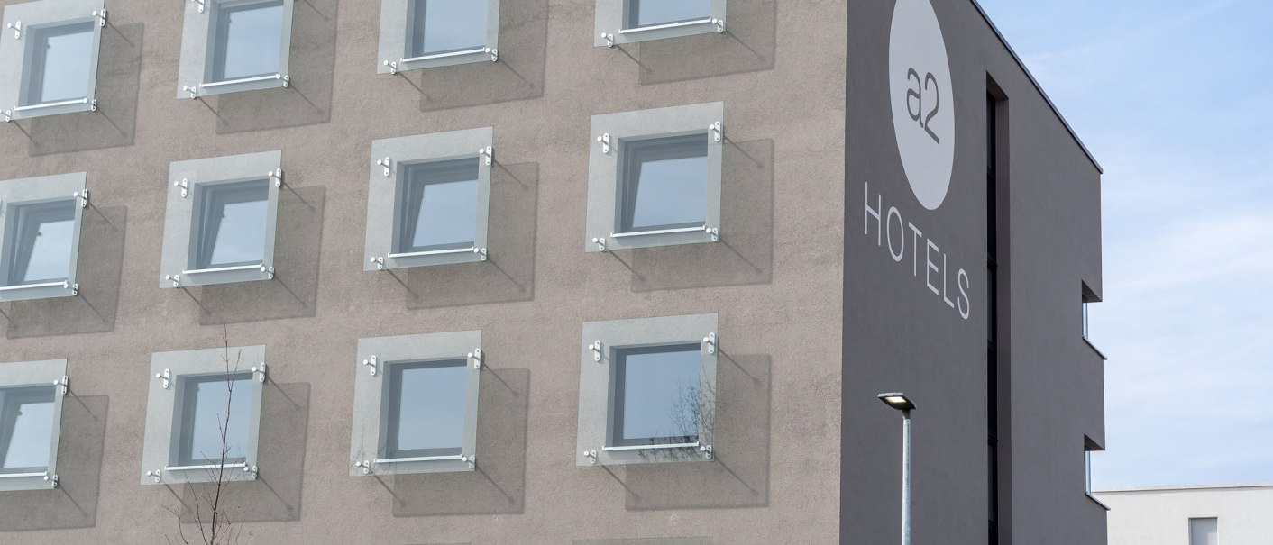 Moderne Hotel-Fassade mit quadratischen Fenstern und dem Logo von a2 HOTELS in Denkendorf., © a2 HOTELS