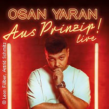 Osan Yaran auf einem Plakat mit dem Titel 'Aus Prinzip! live'. Er steht nachdenklich vor einem roten Hintergrund., &copy; links im Bild