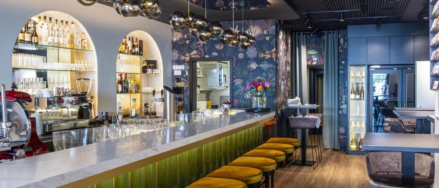 Eleganter Gastraum mit Marmortheke, gelben Hockern und stilvoller Beleuchtung. Die Bar ist gut bestückt, mit Gläsern und Flaschen dekoriert., © SMG, Sarah Schmid