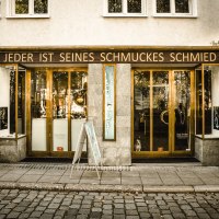 Ein Schmuckgesch&auml;ft mit der Aufschrift 'Jeder ist seines Schmuckes Schmied' &uuml;ber dem Eingang. Die Fassade ist aus Stein, mit gro&szlig;en Fenstern und einer Holzt&uuml;r., &copy; Goldmond