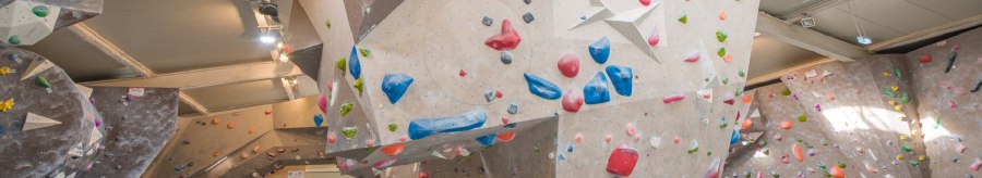 Innenansicht der VELS Boulderhalle mit Kletterwänden und bunten Griffen unter einem gewölbten Dach., © Boulderhalle Vels