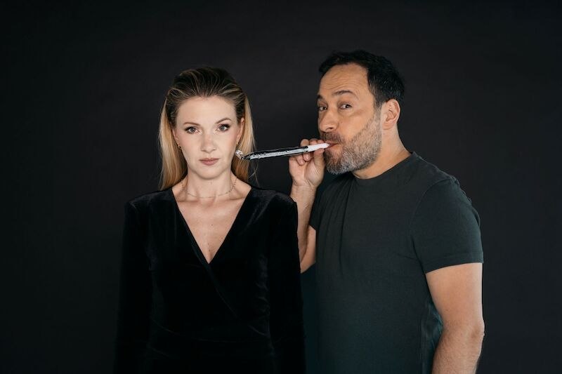 Eine Frau in schwarzem Kleid schaut ernst, während ein Mann neben ihr eine Partytröte bläst. Hintergrund ist schwarz., © Theaterhaus Stuttgart e.V. Eine Frau in schwarzem Kleid schaut ernst, während ein Mann neben ihr eine Partytröte bläst. Hintergrund ist schwarz., © Theaterhaus Stuttgart e.V.