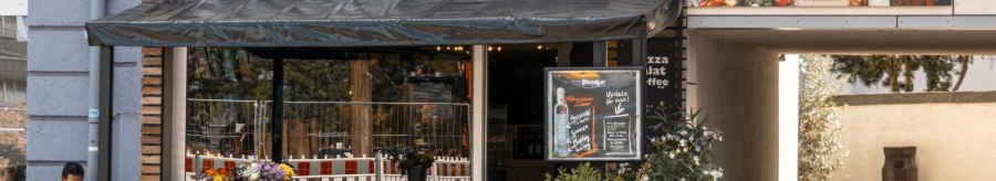 Außenansicht einer Pizzabar mit Terrasse, Blumen und einem Werbeplakat. Ein Mann sitzt an einem Tisch. Die Markise ist schwarz., © Stuttgart Marketing GmbH, Sarah Schmid Außenansicht einer Pizzabar mit Terrasse, Blumen und einem Werbeplakat. Ein Mann sitzt an einem Tisch. Die Markise ist schwarz., © Stuttgart Marketing GmbH, Sarah Schmid