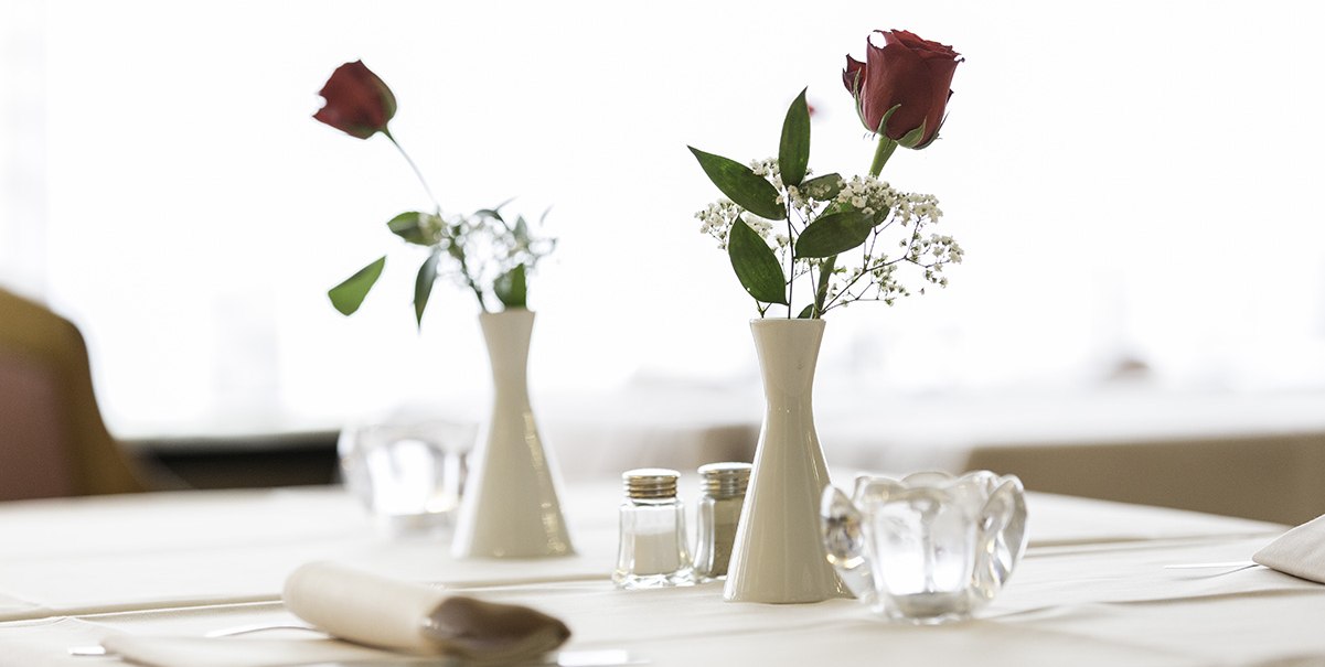Gedeckter Tisch mit weißen Tischdecken, zwei Vasen mit roten Rosen, Salz- und Pfefferstreuer in einem Restaurant., © Hotel Royal