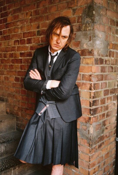 Person in a dark suit and kilt, arms folded, standing in front of a brick wall., &copy; C2 Concerts GmbH