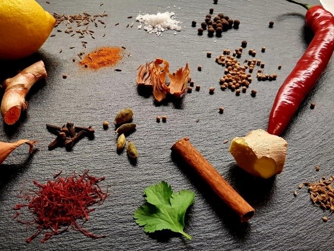 Eine Auswahl an Gew&uuml;rzen und Zutaten, darunter Zitrone, Chili, Ingwer, Zimt, Kardamom und Safran, auf einer dunklen Oberfl&auml;che arrangiert., &copy; Kultweine-Kochwelten-Kunst&uuml;cke - Kochschule Sonja Lenz