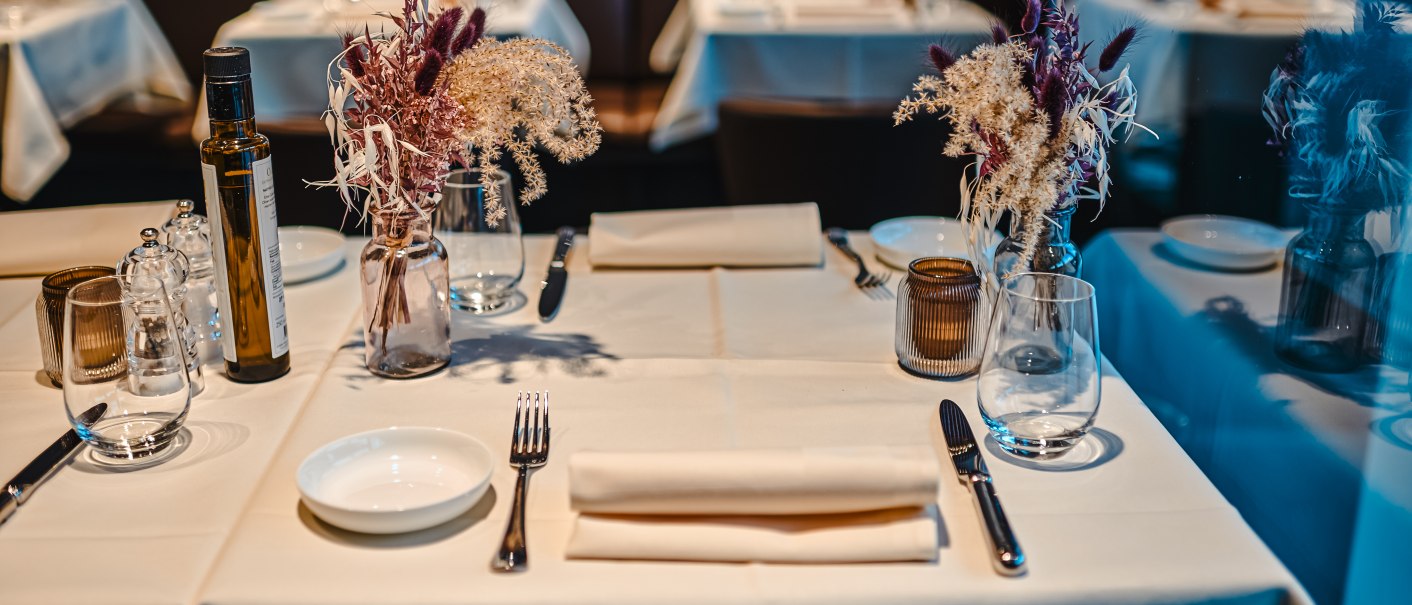 An elegantly laid table in a restaurant with white tablecloths, flower arrangements, glasses and cutlery., © Feinkost Böhm GmbH An elegantly laid table in a restaurant with white tablecloths, flower arrangements, glasses and cutlery., © Feinkost Böhm GmbH