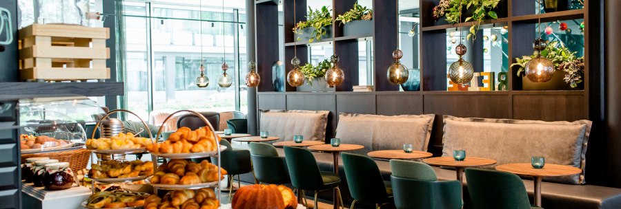 Elegantes Fr&uuml;hst&uuml;cksbuffet mit Croissants, Kuchen und Gem&uuml;se in einem stilvollen Restaurant mit gr&uuml;nen St&uuml;hlen und h&auml;ngenden Lampen., &copy; Motel One - Stuttgart Hauptbahnhof