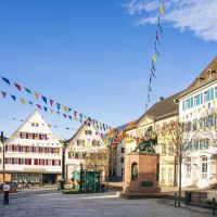 The town square in Weil der Stadt features historic buildings and colorful pennants against a blue sky. A statue stands in the center of the square., &copy; SMG Stuttgart Marketing GmbH - Sarah Schmid