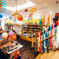 Ein bunter Spielzeugladen mit Regalen voller Spielsachen, Kleidung und Dekorationen. Bunte Schals und Spielzeuge sind prominent ausgestellt., &copy; 1000sch&ouml;n