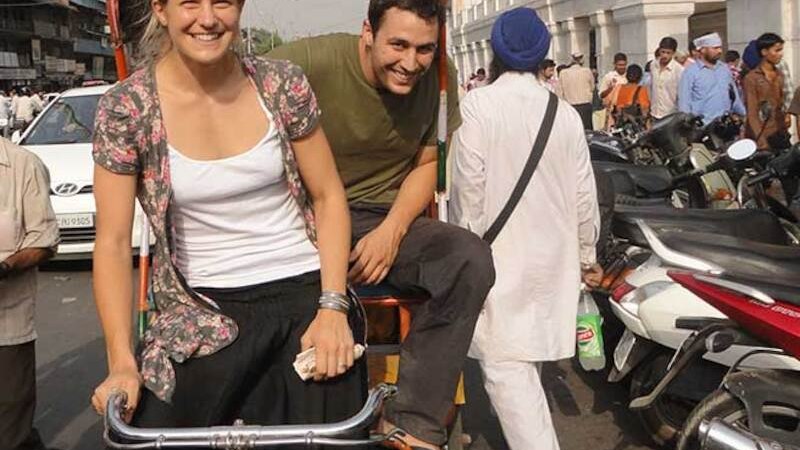 Zwei Personen sitzen fr&ouml;hlich auf einer Rikscha in einer belebten Stra&szlig;e voller Menschen und Motorr&auml;der., &copy; Theaterhaus Stuttgart e.V.