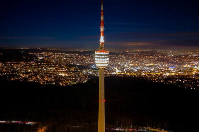 Der Fernsehturm steht beleuchtet in der Nacht, umgeben von der erleuchteten Stadt im Hintergrund. Der Himmel ist dunkelblau., © SWR Media Services GmbH / SWR Fernsehturm Stuttgart