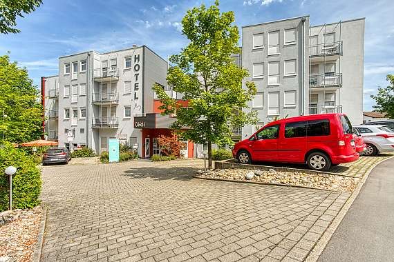 Das Centro Hotel U-NO1 zeigt eine moderne Fassade mit Balkonen. Vor dem Gebäude sind Autos geparkt, umgeben von Bäumen und einem gepflasterten Weg., © Centro Hotels