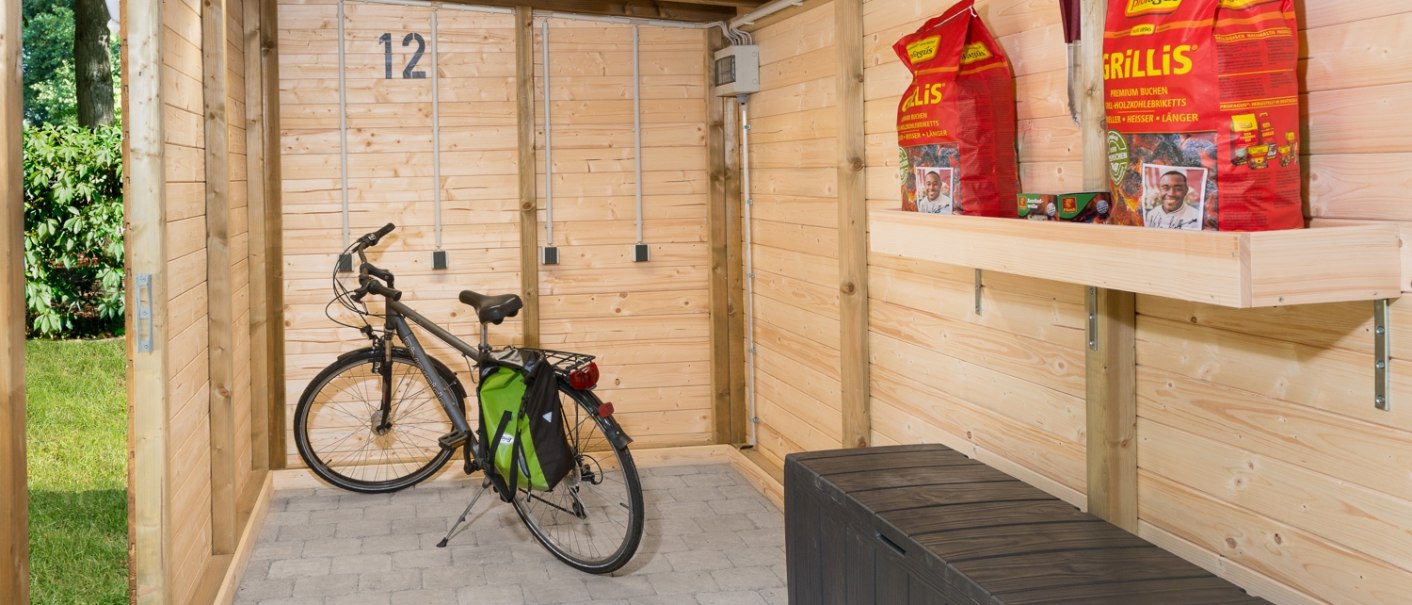 Holzschuppen mit Fahrrad, grüner Fahrradtasche, Grillkohle auf einem Regal und einer schwarzen Aufbewahrungsbox. Nummer 12 an der Wand., © Remsfässer