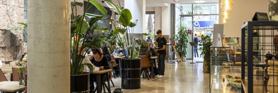 Modern café with large plants, tables and a waiter. People sit and enjoy their time. Bright, inviting atmosphere., © SMG Stuttgart Marketing GmbH - Sarah Schmid