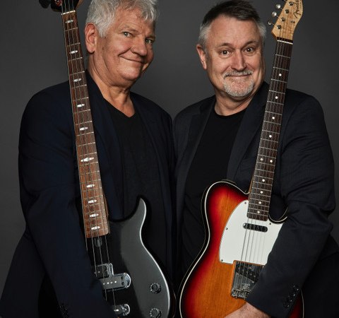 Zwei M&auml;nner in dunkler Kleidung halten E-Gitarren vor einem grauen Hintergrund und l&auml;cheln in die Kamera., &copy; Renitenztheater Stuttgart e.V.