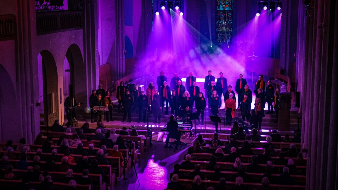 Ein Chor tritt in einer Kirche auf, beleuchtet von lila Scheinwerfern. Die Zuschauer sitzen in Kirchenb&auml;nken und lauschen dem Gesang., &copy; Chorisma Cannstatt
