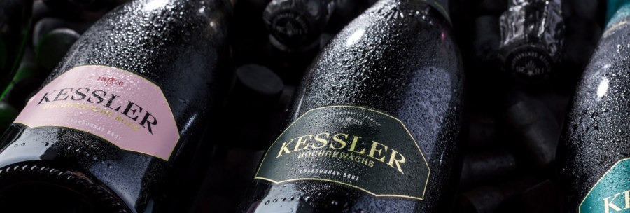 Nahaufnahme von Kessler Sektflaschen, bedeckt mit Wassertropfen. Die Etiketten zeigen verschiedene Sorten wie Rosé und Chardonnay Brut., © KESSLER Sekt GmbH & Co. KG