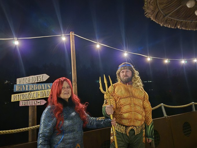 Zwei verkleidete Personen stehen auf einem Bootssteg unter Lichterketten. Eine trägt ein Aquaman-Kostüm, die andere ein Meerjungfrauen-Kostüm., © Cool-Tours StattReisen Zwei verkleidete Personen stehen auf einem Bootssteg unter Lichterketten. Eine trägt ein Aquaman-Kostüm, die andere ein Meerjungfrauen-Kostüm., © Cool-Tours StattReisen