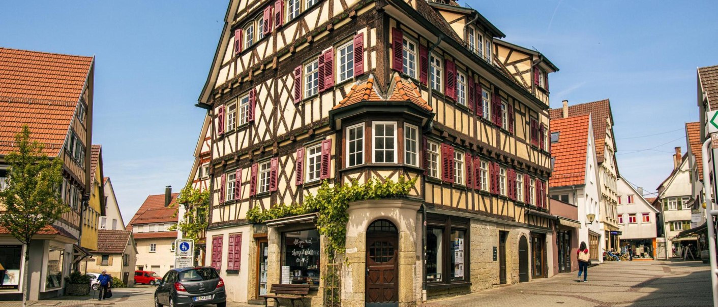 Half-timbered house in the old town of Herrenberg with red shutters and a bay window. People walk along the cobbled street., © Stuttgart-Marketing GmbH, Sarah Schmid