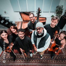 Gruppe von sieben Musikern mit Instrumenten steht in einem Raum mit Flügel. Sie blicken nach oben zur Kamera., © links im Bild Gruppe von sieben Musikern mit Instrumenten steht in einem Raum mit Flügel. Sie blicken nach oben zur Kamera., © links im Bild