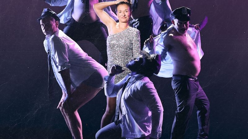 A woman in a glittering dress poses with five men in police uniforms in front of a purple background. The men dance and pose in various poses., &copy; Theaterhaus Stuttgart e.V.