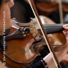 Nahaufnahme einer Geige, die von einer Person im Orchester gespielt wird. Der Fokus liegt auf den Saiten und dem Bogen., © links im Bild Nahaufnahme einer Geige, die von einer Person im Orchester gespielt wird. Der Fokus liegt auf den Saiten und dem Bogen., © links im Bild