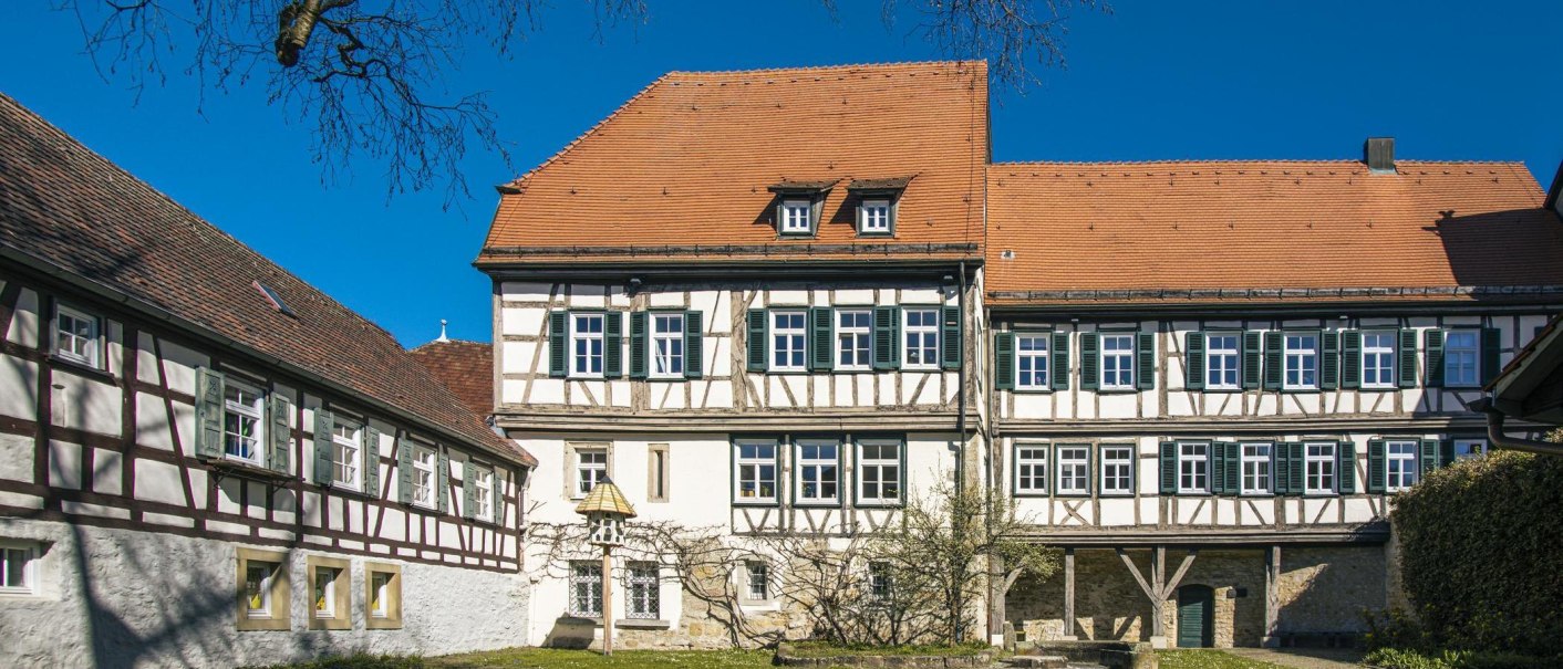 A half-timbered building belonging to the Sindelfingen Deanery, with a red-tiled roof and blue shutters. The sky is clear and blue., © SMG Stuttgart Marketing GmbH - Sarah Schmid A half-timbered building belonging to the Sindelfingen Deanery, with a red-tiled roof and blue shutters. The sky is clear and blue., © SMG Stuttgart Marketing GmbH - Sarah Schmid