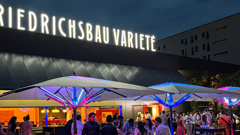 Abendliche Szene vor dem Friedrichsbau Variet&eacute; mit beleuchteten Sonnenschirmen und Menschen, die sich unterhalten und entspannen., &copy; Friedrichsbau Variet&eacute;