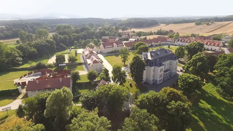 Luftaufnahme von Kreisau/Krzyżowa zeigt historische Geb&auml;ude umgeben von gr&uuml;ner Landschaft und Feldern., &copy; Krzyżowa-Music/Musik aus Kreisau. F&uuml;r Europa.