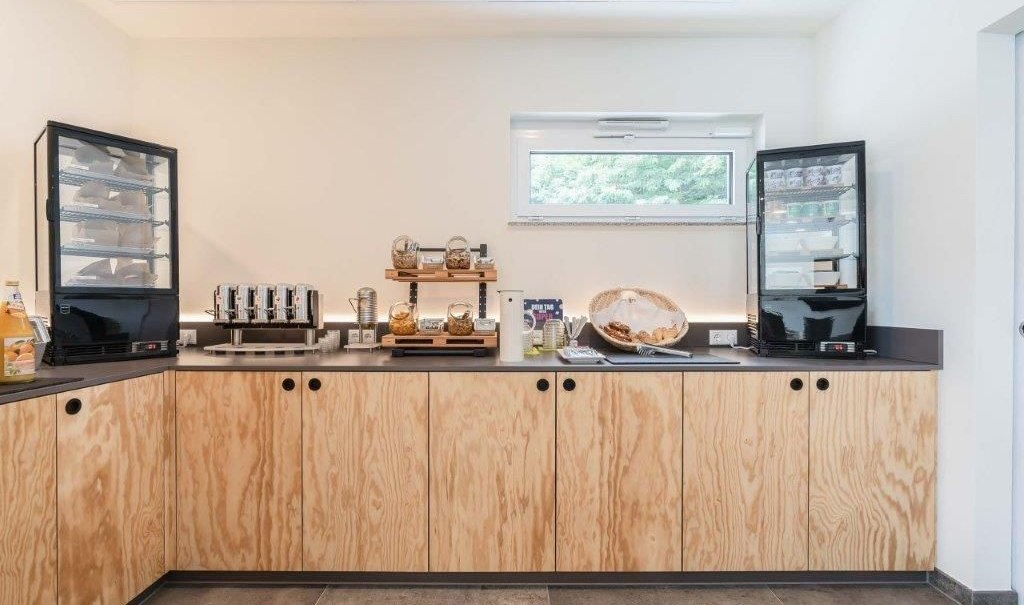 A breakfast buffet with bread baskets, a coffee maker, and beverages on a wooden counter in a bright room., &copy; a2 HOTELS am Quadrium