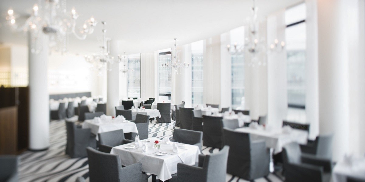 Elegantes Restaurant mit weißen Tischdecken, grauen Stühlen und Kronleuchtern. Große Fenster lassen viel Licht herein., © Mövenpick Hotel Stuttgart Airport Elegantes Restaurant mit weißen Tischdecken, grauen Stühlen und Kronleuchtern. Große Fenster lassen viel Licht herein., © Mövenpick Hotel Stuttgart Airport
