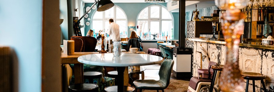 Cozy caf&eacute; with stylish furnishings, round tables and chairs. People sit and chat. Large windows let in light., &copy; SMG Stuttgart Marketing GmbH - Sarah Schmid